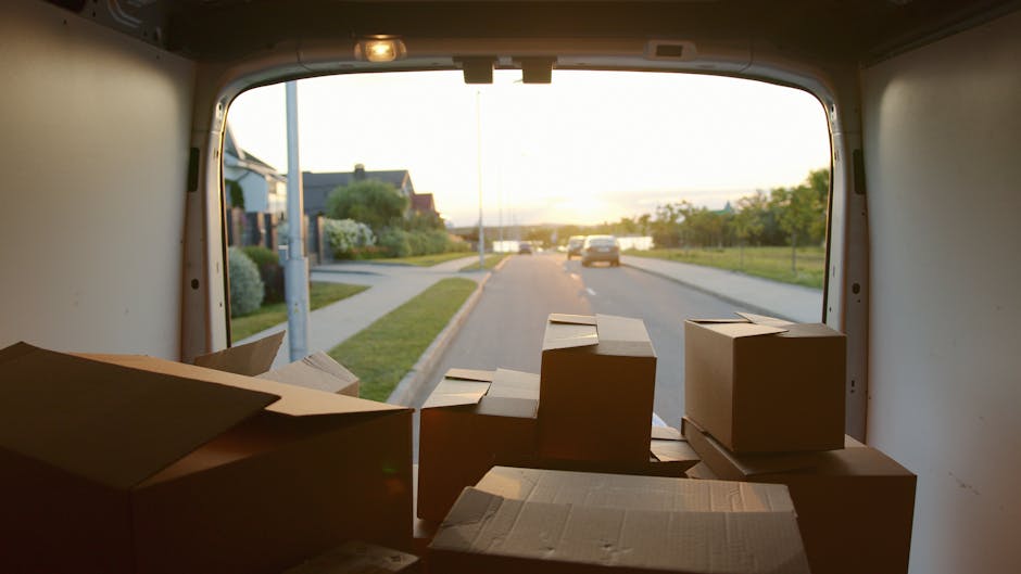 A white moving van parked outdoors on a paved area during daytime, with a portion of the side panel visible displaying the text 'MOVING COMPANY' and 'LOCAL & LONG DISTANCE' in bold dark letters. The v